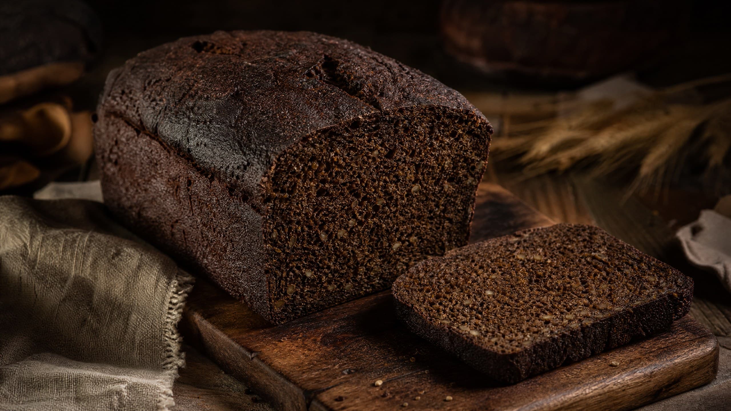 Freshly baked sourdough pumpernickel bread: dark, dense, deep rye, photographed on a warm cream background