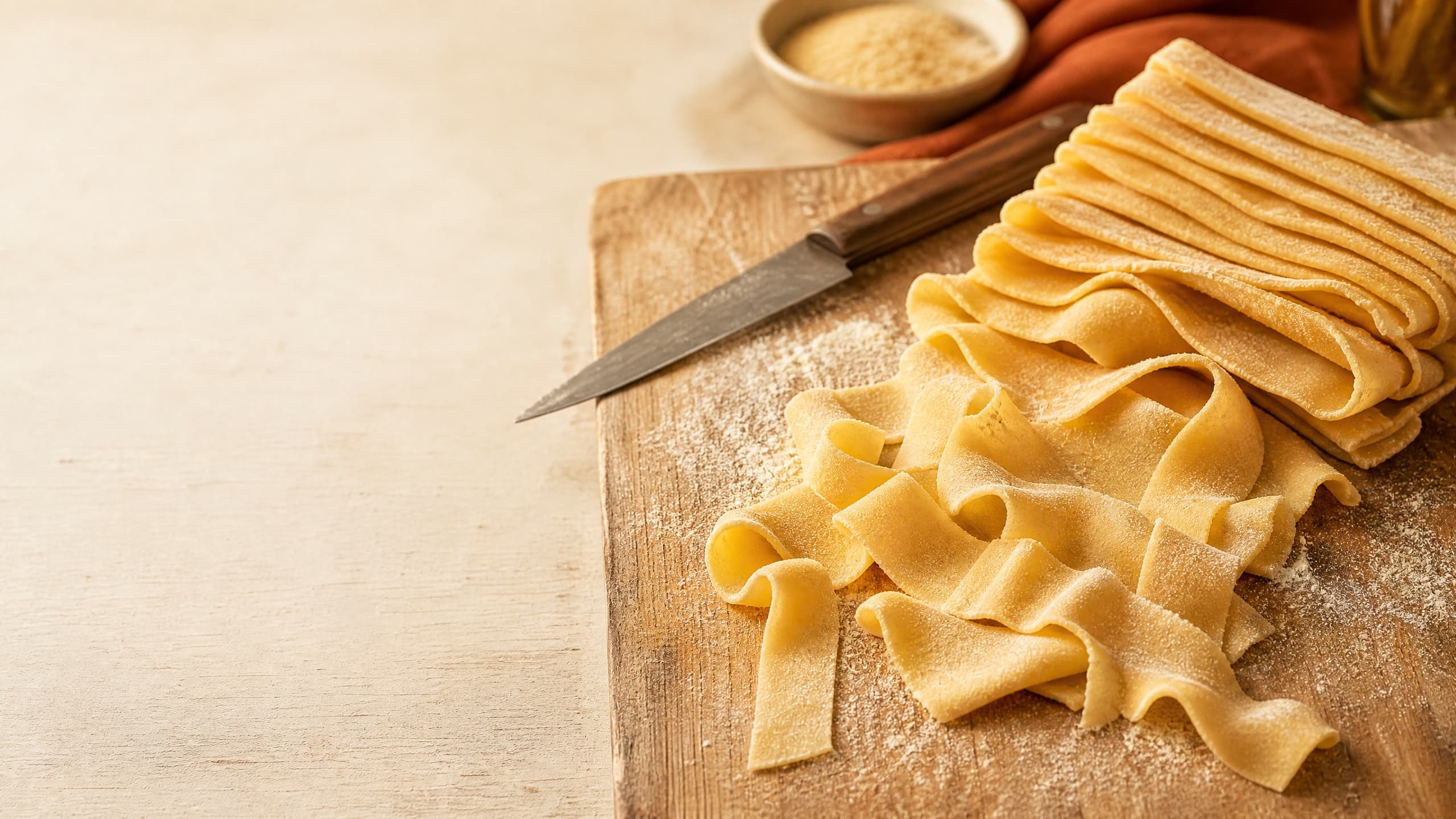 Freshly baked homemade pappardelle pasta (wide hand-cut ribbons), photographed on a warm cream background