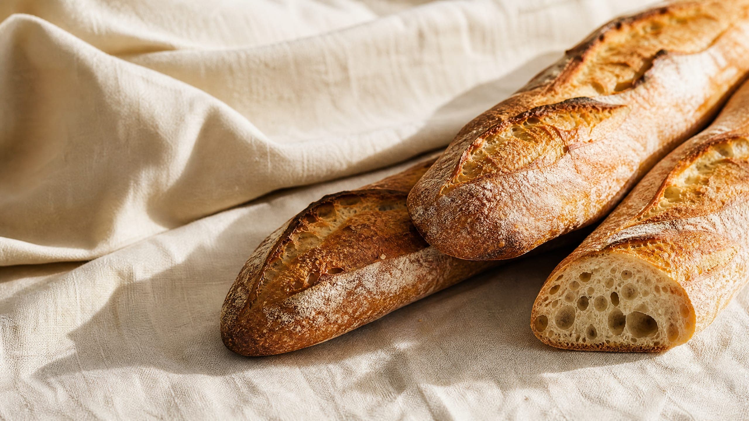 Freshly baked sourdough baguette, photographed on a warm cream background